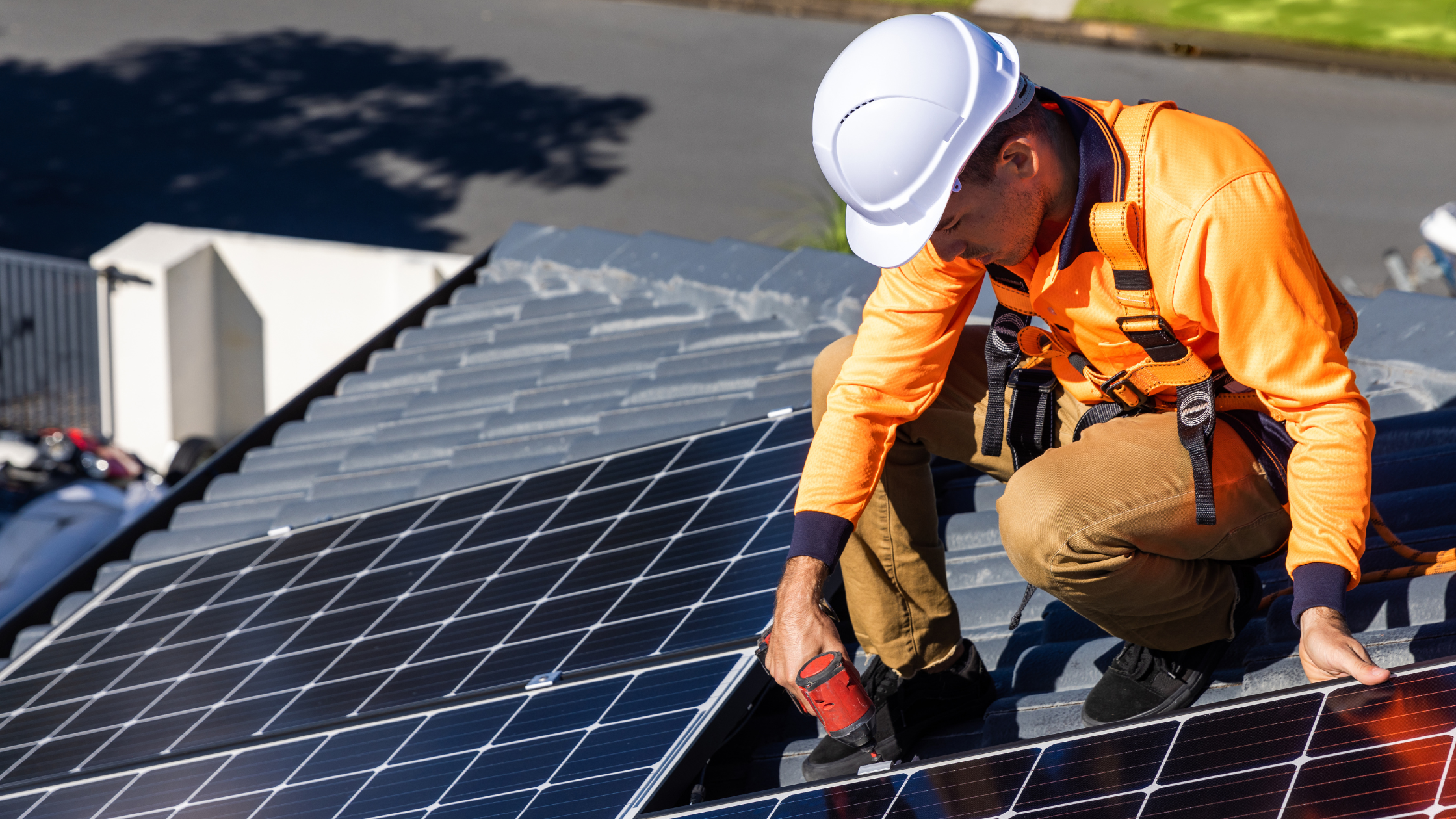 Solar technician in safety gear repairing rooftop solar panels with a power drill.